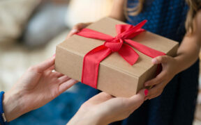 Junges Mädchen übergibt Geschenk mit beiden Händen