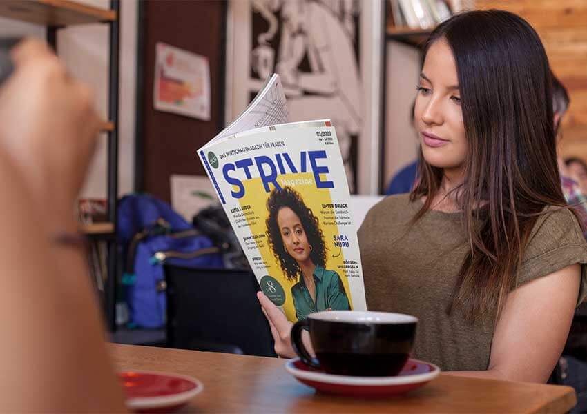 Junge Frau liest im Café im STRIVE Magazine.