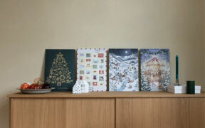 Vier Foto-Adventskalender der kartenmacherei stehen nebeneinander auf einer Holzkommode.