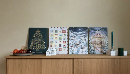 Vier Foto-Adventskalender der kartenmacherei stehen nebeneinander auf einer Holzkommode.