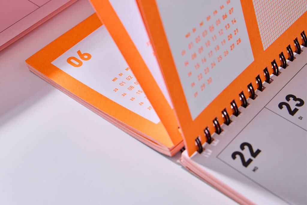 Neonorangener Tischkalender 2027 von Fox & Poet mit aufgeschlagenen Kalenderseiten