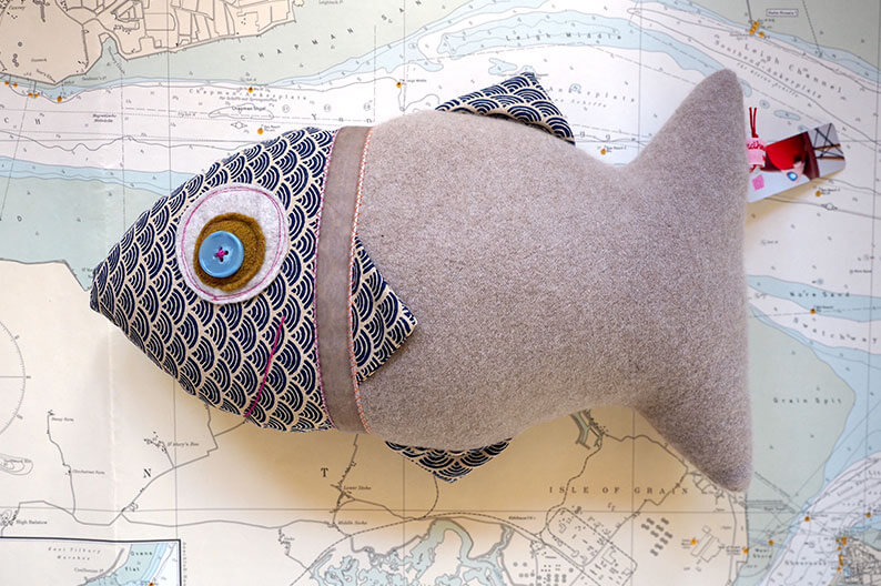Ein handgenähtes Fischkissen aus verschiedenen Stoffen liegt auf einer Landkarte.