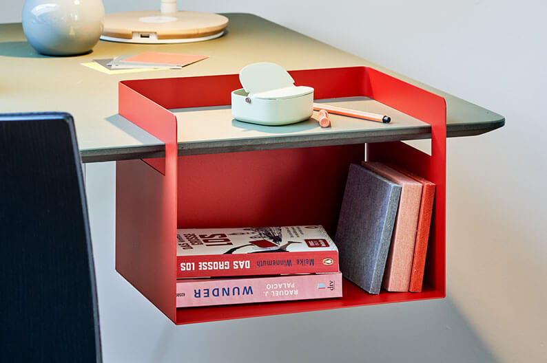 Rote Aufbewahrungsbox hängt an einer Tischplatte und enthalten Bücher und kleine Gegenstände.