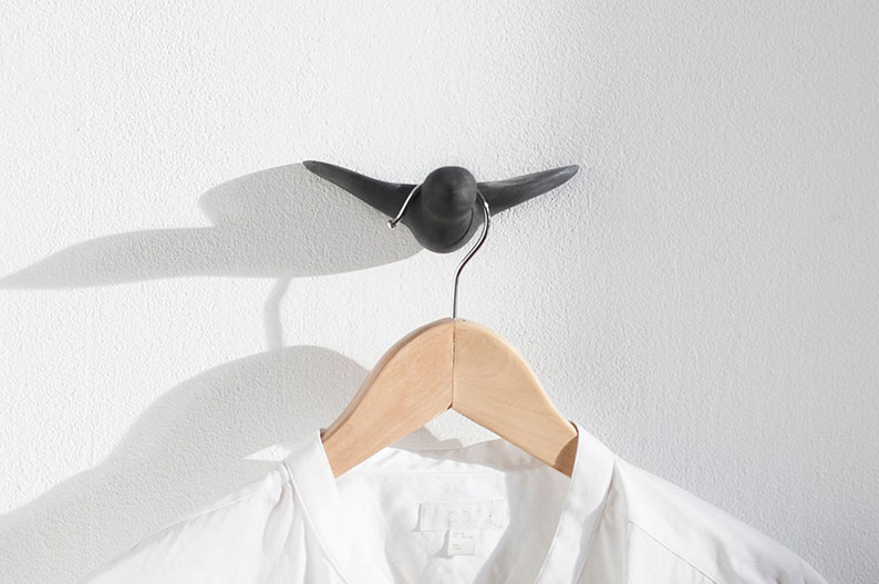Schwarzer Vogel-Wandhaken an einer weißen Wand mit einem aufgehängten Kleiderbügel und Hemd.