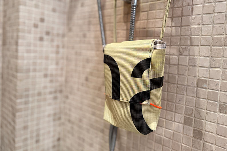 Eine hängende Duschtasche mit Pflegeprodukten befindet sich an einer gefliesten Wand.