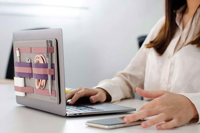 Eine Frau arbeitet an einem Laptop, auf dessen Rückseite ein rosafarbener Organizer befestigt ist.