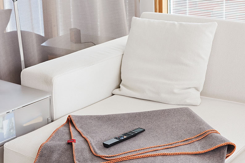 Graue Kuscheldecke von ASK THE FOX liegt zusammengefaltet auf einem weißen Sofa.